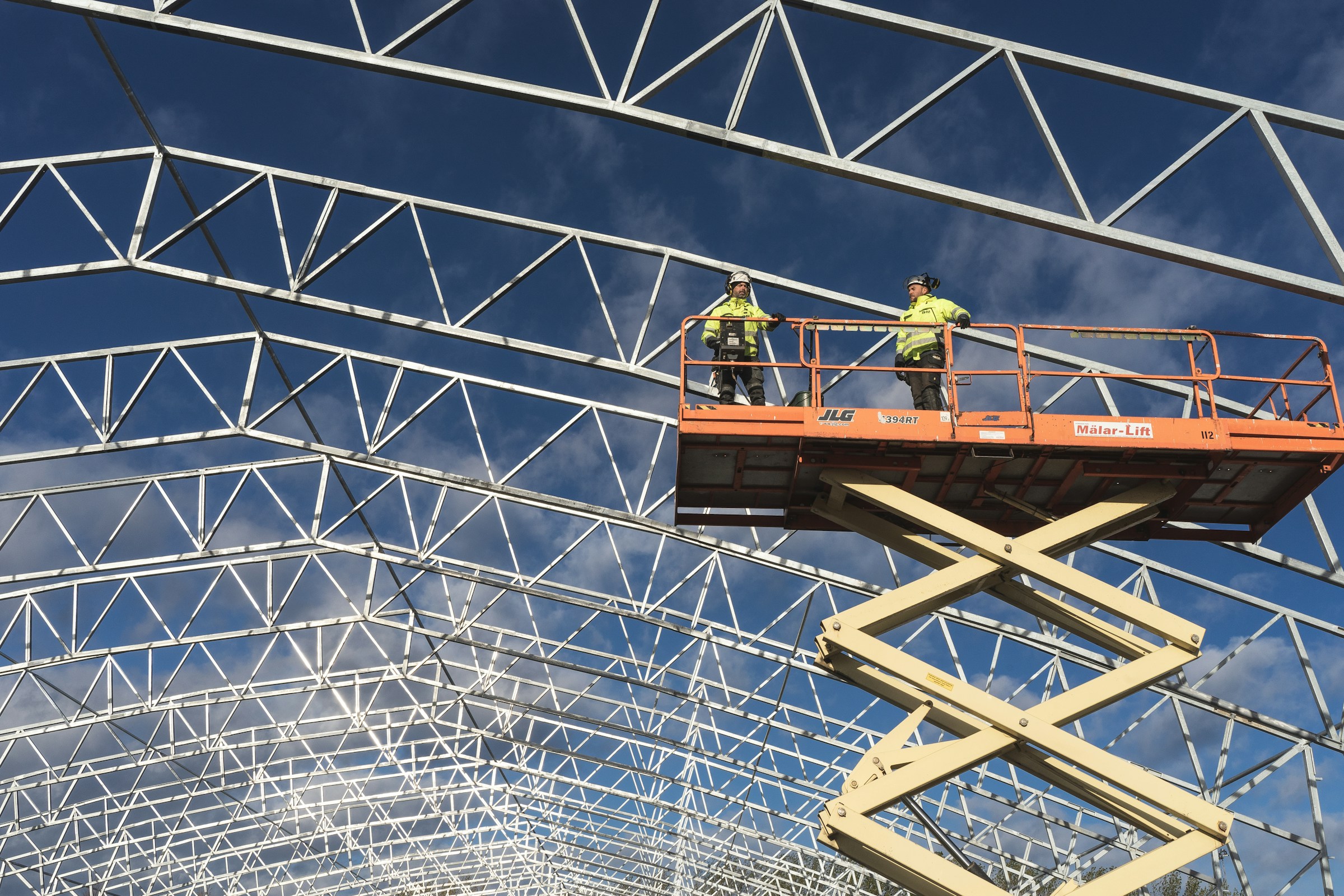 Construction workers operating a scissor lift beneath a steel roof structure